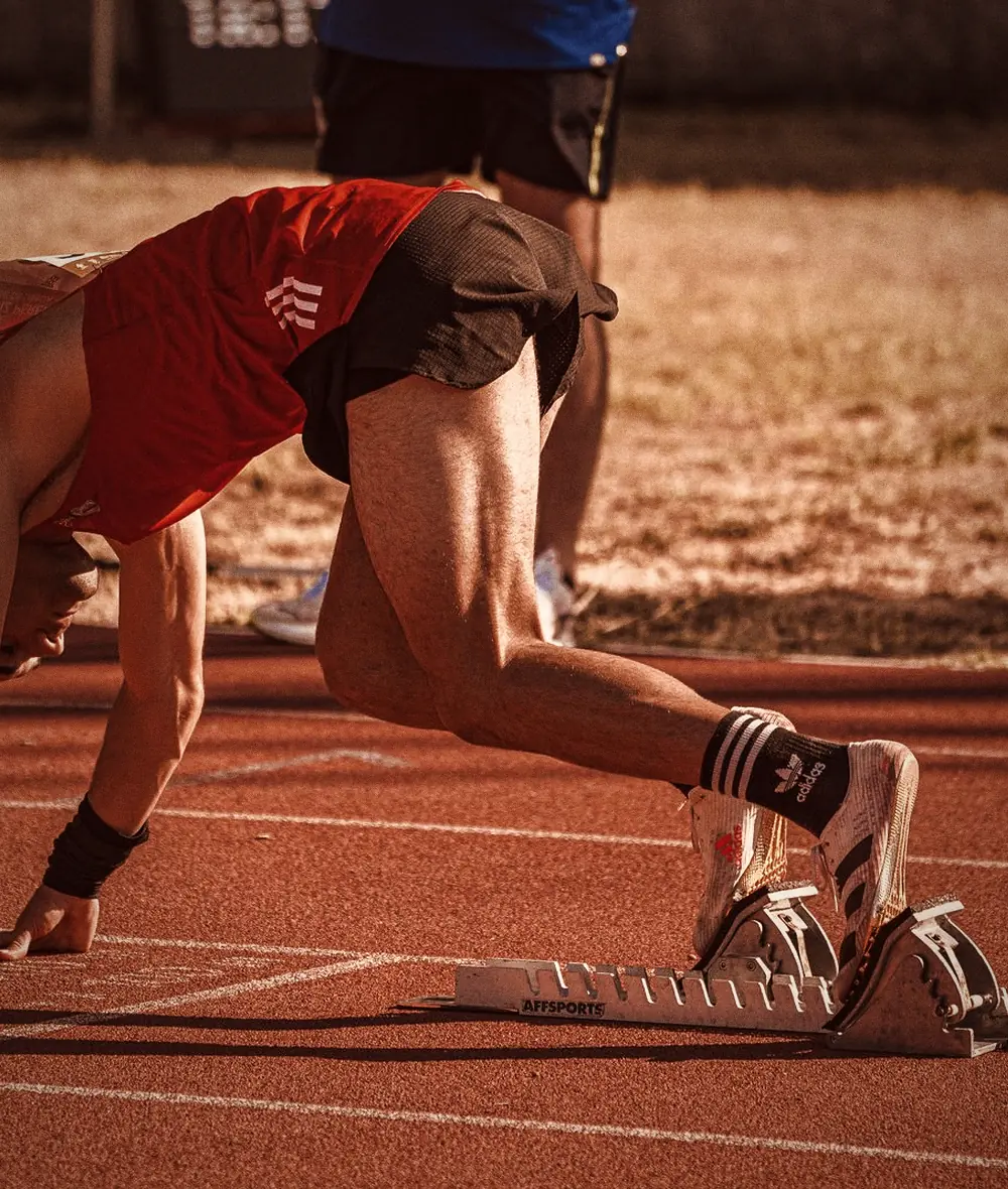 A sprinter drives out of the blocks on a red track